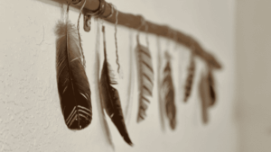 Feathers hanging from a wooden stick, symbolizing spiritual connection, shamanic tools, and communication with the unseen realms