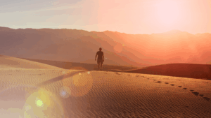 Person walking alone across desert dunes at sunrise, symbolizing a vision quest and spiritual rite of passage