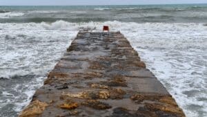 A red chair on a stone pier overlooking the ocean, symbolizing trust and deep connections amidst crashing waves.