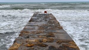 A red chair on a stone pier overlooking the ocean, symbolizing trust and deep connections amidst crashing waves.