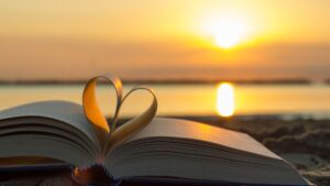 Open book with pages forming a heart shape against the backdrop of a sunset over calm waters, symbolizing self-love lessons from loss.