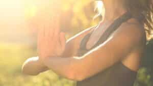 A woman practicing meditation outdoors in warm sunlight, hands in prayer position, symbolizing trust, clarity, and spiritual alignment.