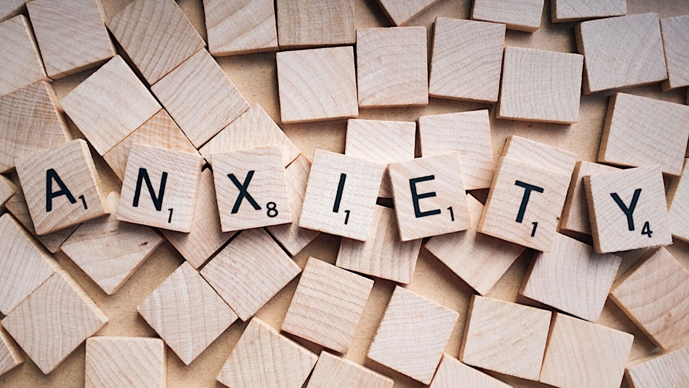Wooden letter tiles spelling the word anxiety, representing the hidden patterns and deeper causes behind anxiety and emotional distress.
