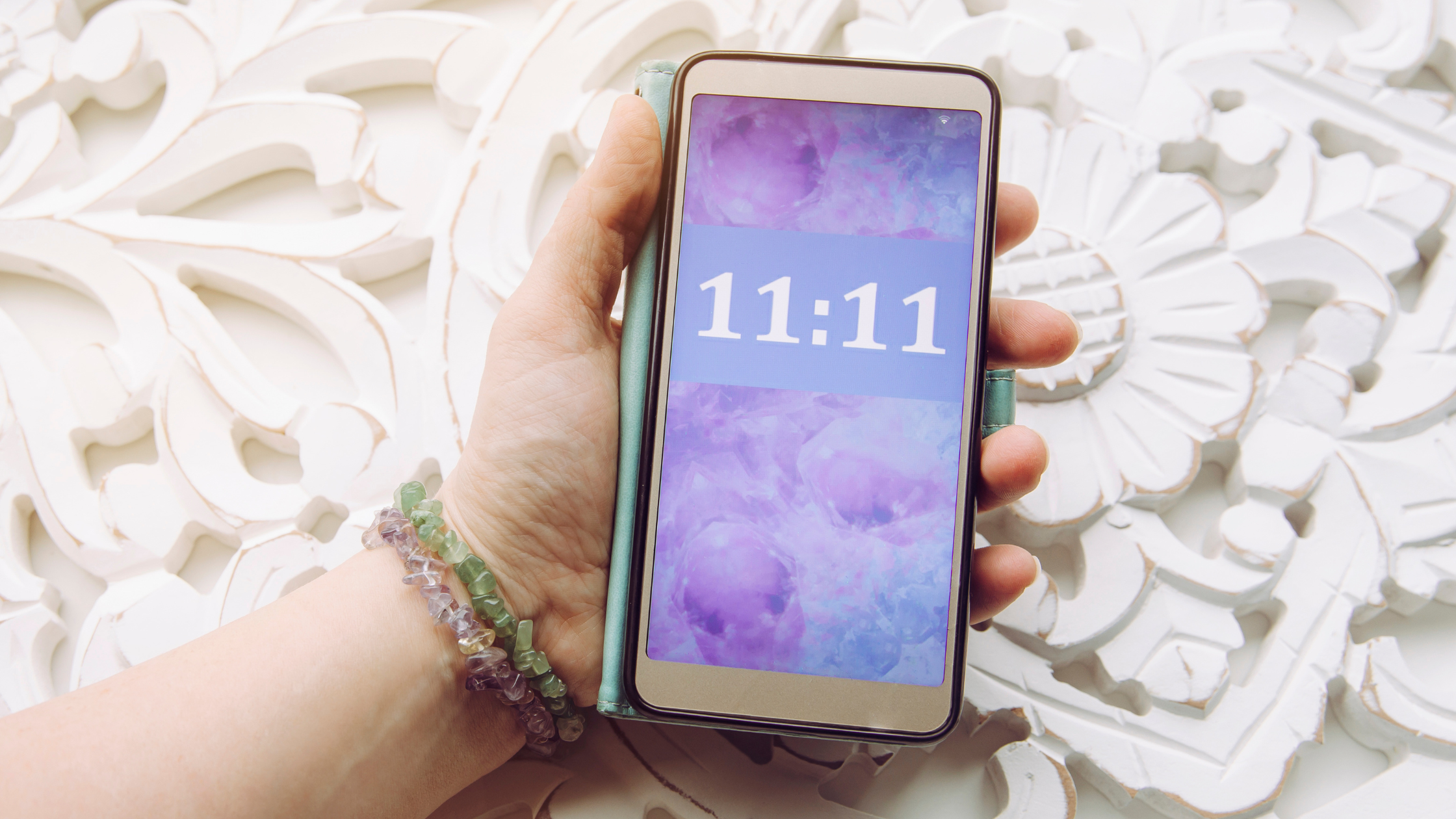 Hand holding phone showing 11:11 synchronicity next to crystals, illustrating how spirit speaks through dreams, symbols and synchronicities