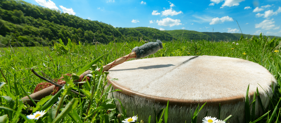 Shamanic drum with grass and blue sky. Hero image for post on Shamanic Journey and Psychedlics