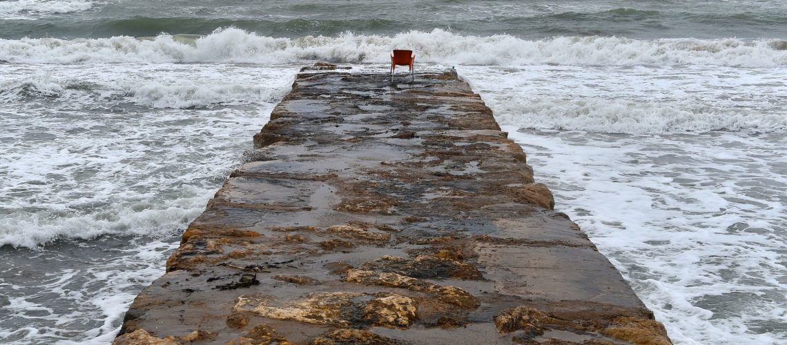 A red chair on a stone pier overlooking the ocean, symbolizing trust and deep connections amidst crashing waves.