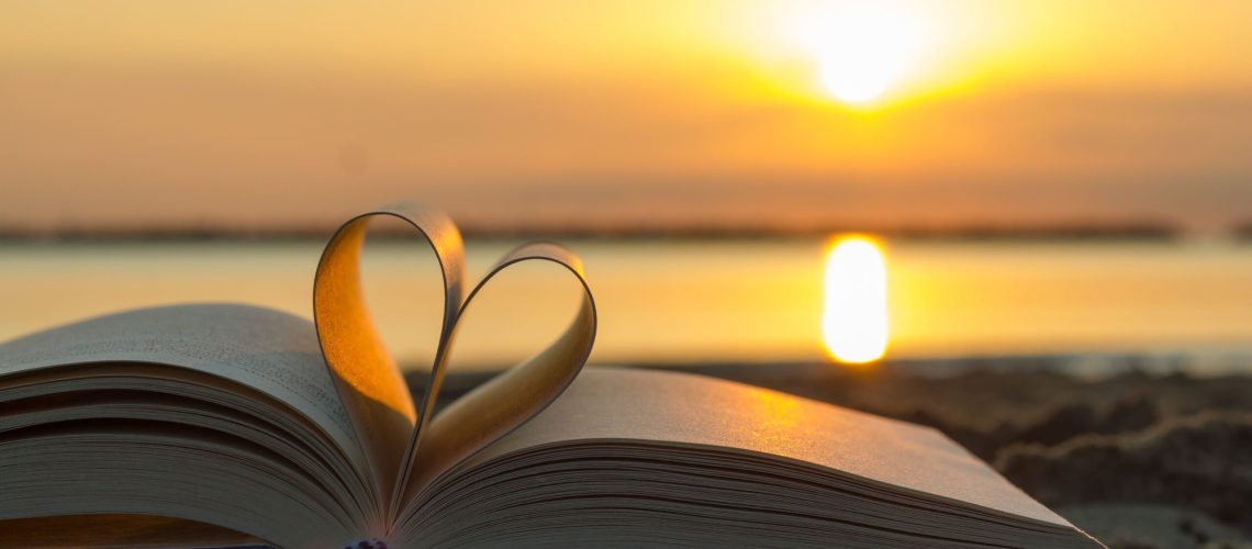 Open book with pages forming a heart shape against the backdrop of a sunset over calm waters, symbolizing self-love lessons from loss.